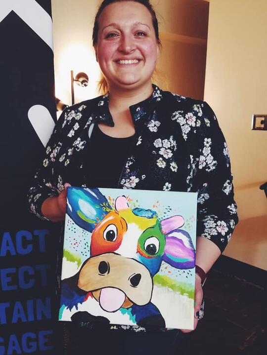 Hannah holding a colorful painting at a paint night event